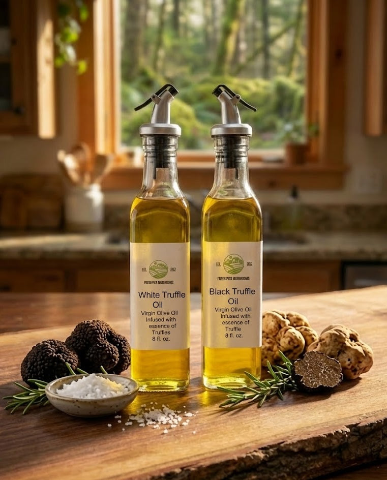 Two bottles of Fresh Pick Mushrooms White Truffle Oil and Black Truffle Oil with pour spouts, resting on a rustic live-edge wooden slab counter alongside fresh black and white truffles, a bowl of coarse salt, and rosemary sprigs in a sunlit kitchen with a forest view.